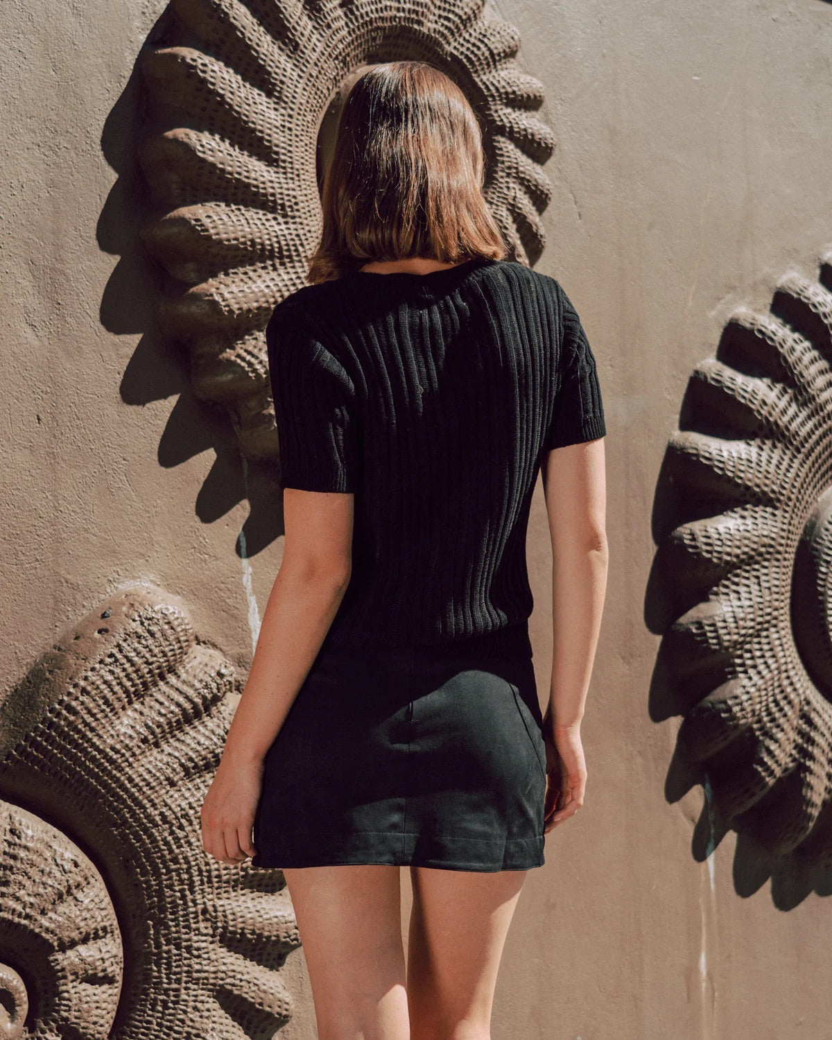 Person wearing a black outfit standing in front of large decorative wall art.