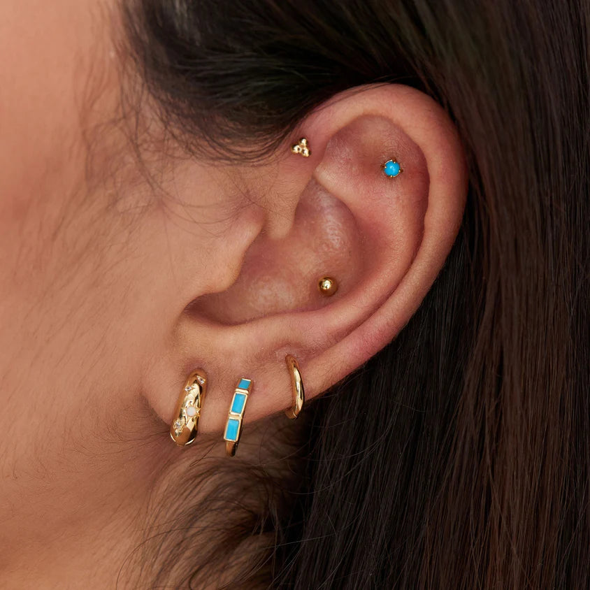 Close-up of an ear with multiple gold and turquoise earrings.