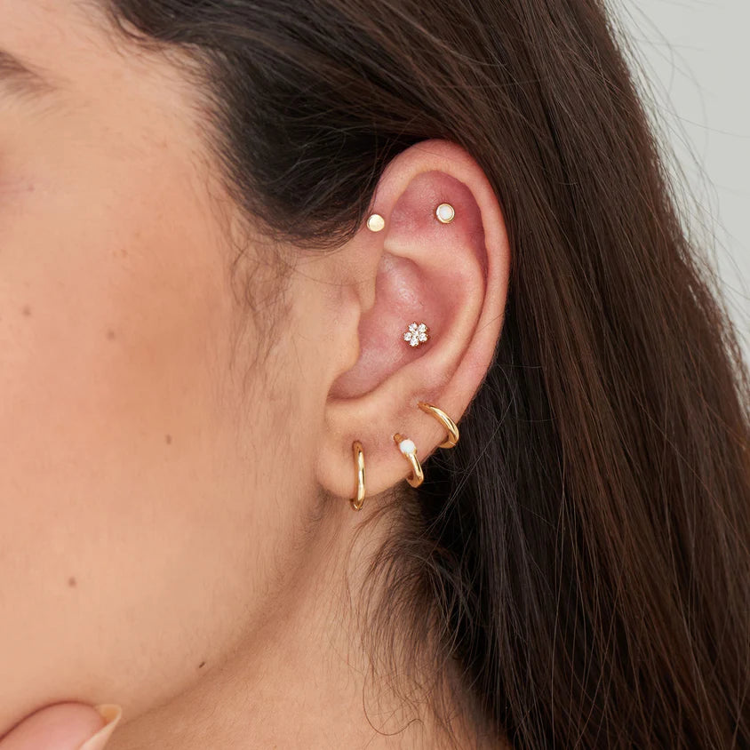 Close-up of an ear with gold earrings and a small flower-shaped earring.