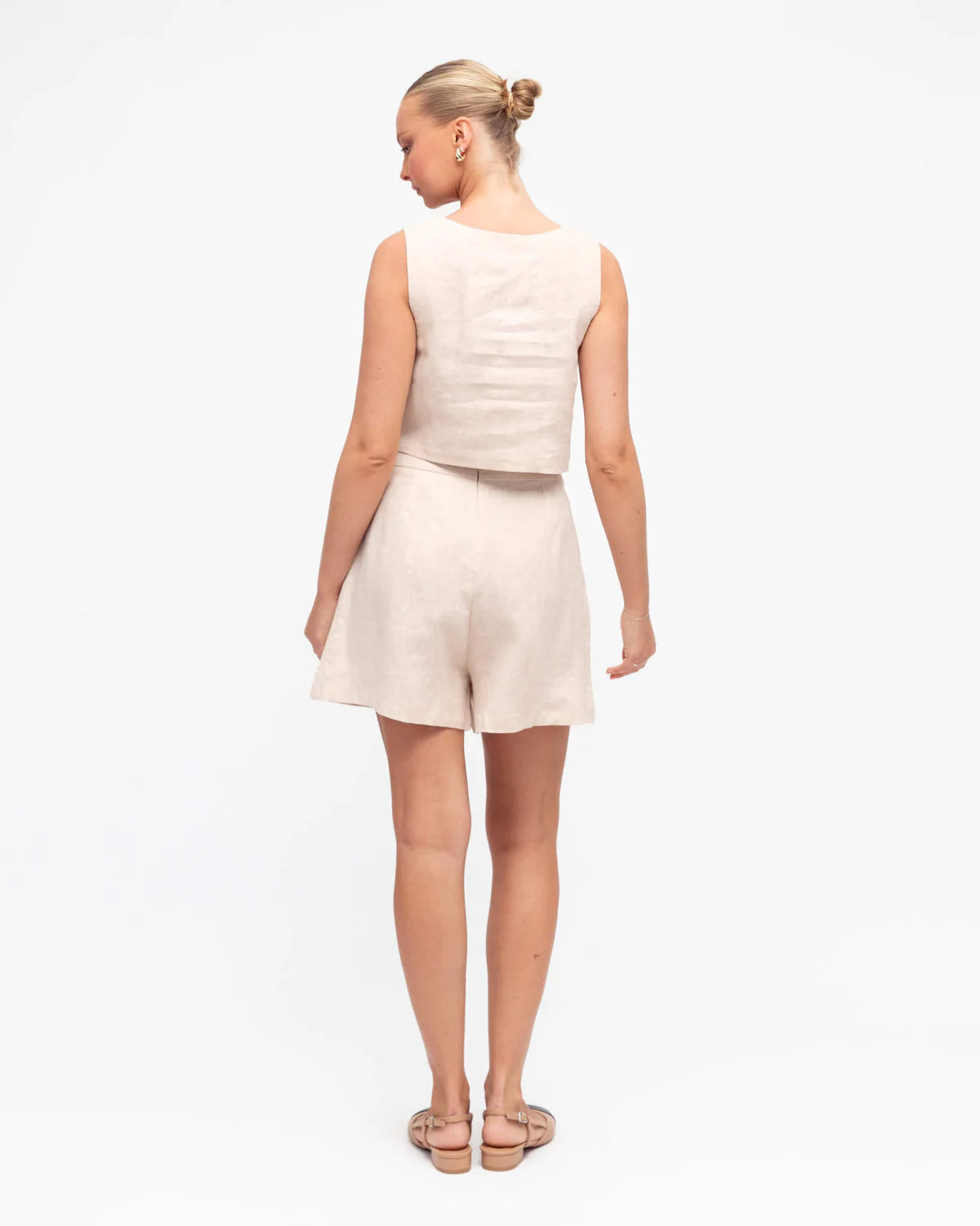 Woman wearing a sleeveless beige top and shorts on a white background