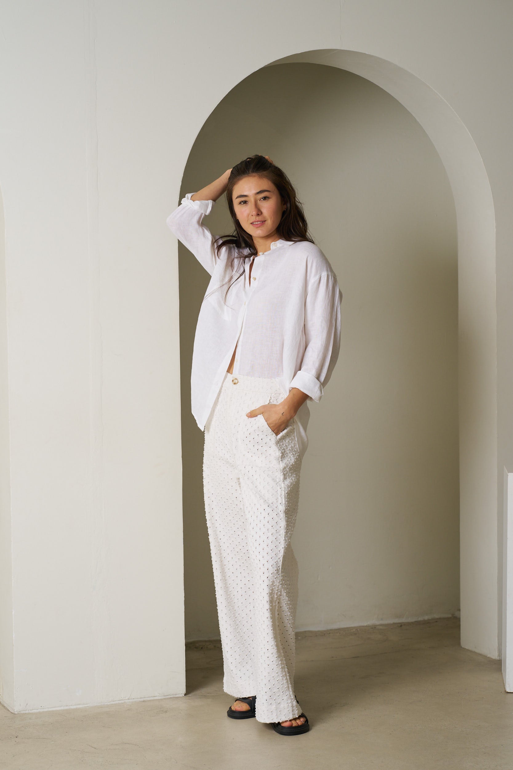 Woman in a white outfit standing in an archway with a neutral background